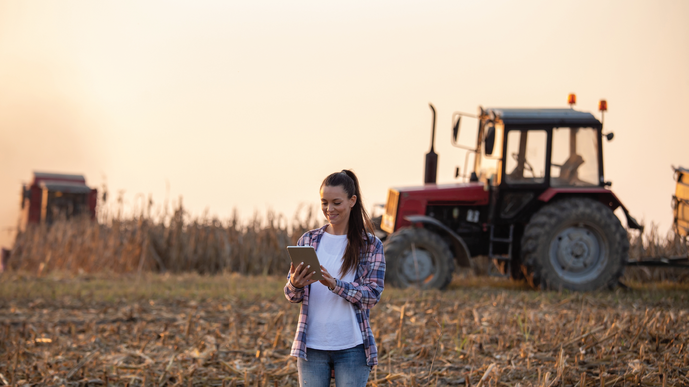 Woman walking on farm with a phone in her hand and a tractor in the background