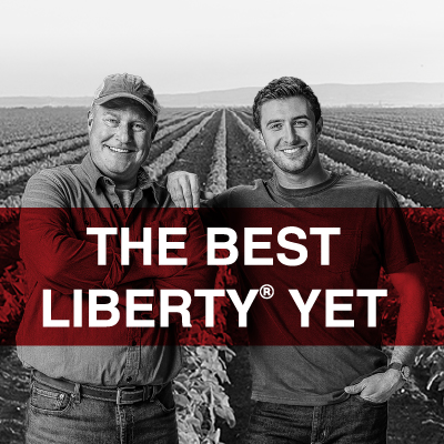 A black and white image of a soybean field with a man in his 60s smiling with arms crossed and his son in his 30s in front of the field. The son is leaning on the father with his hand on his shoulder.