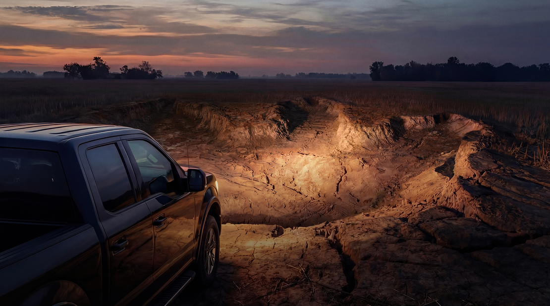 A truck in a field at night with its headlights focused on a dinosaur footprint