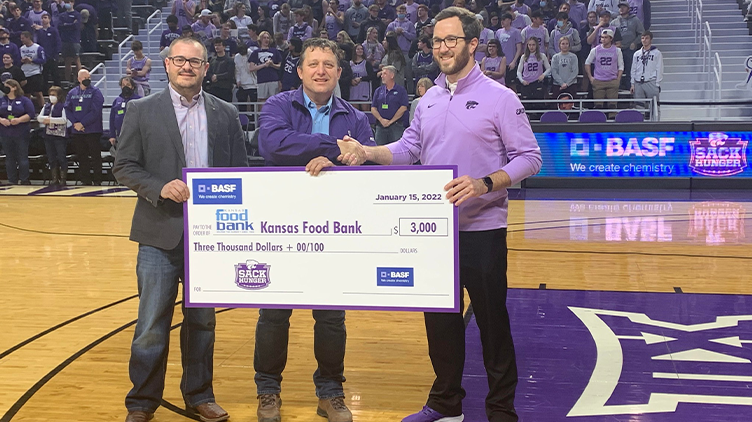 Three men holding a giant check in basketball gym
